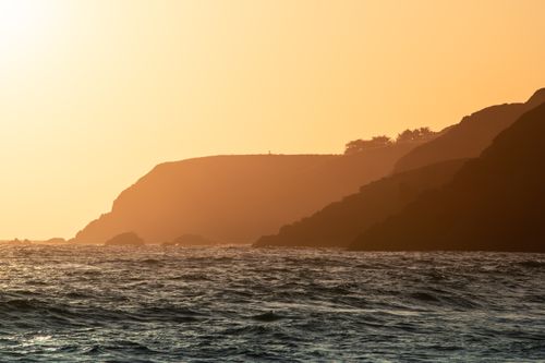 Free Gorgeous coastal view with cliff silhouettes and gentle waves at sunset, exuding a serene and warm atmosphere. Stock Photo