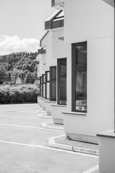 A black and white photo of contemporary building facades with empty parking spaces in front.