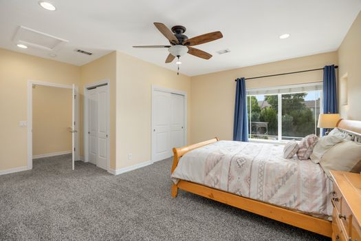 Spacious bedroom featuring a comfortable bed and ceiling fan with natural light.