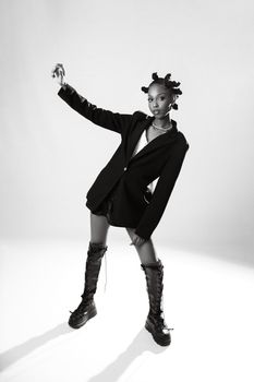 Elegant woman posing in a studio wearing a blazer and boots, showcasing modern fashion.