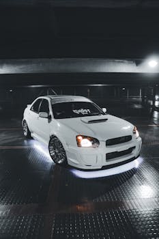 A sleek white Subaru sports car with neon underglow lights in a dimly lit parking garage.