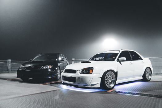 Two customized sedans with neon lights parked at night, highlighting automotive tuning.