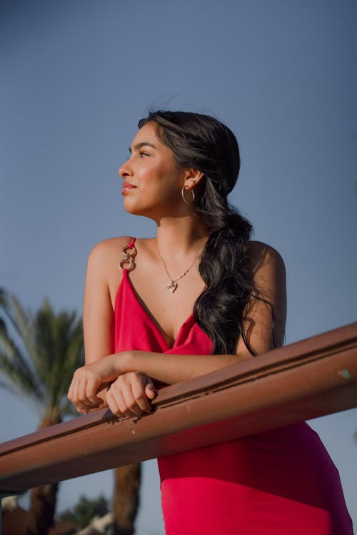 Beautiful Model in Red Dress Posing by Railing on Terrace