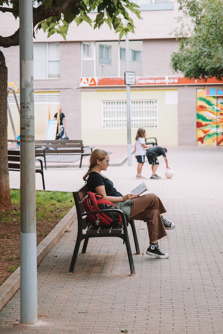 Woman Sitting On Bench And Reading Book