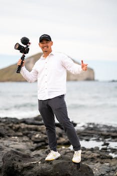 Smiling man with camera on a rocky beach, capturing the scenic ocean view.