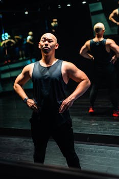 Bald man in sportswear posing confidently in a gym mirror, showcasing fitness and strength.