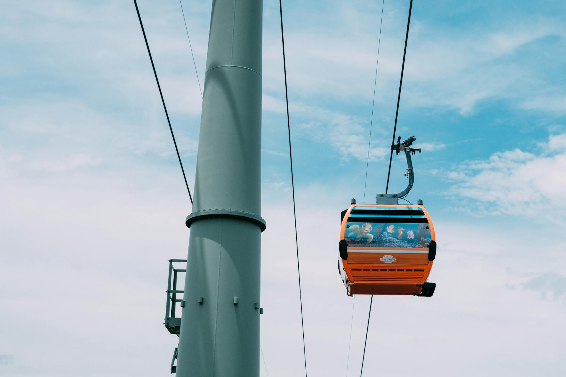 Bright orange gondola lift ascending against a vibrant blue sky, a perfect scene of modern transportation.