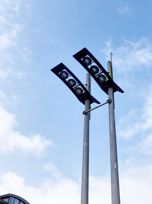 Free Modern floodlights on tall poles set against a bright blue sky. Stock Photo