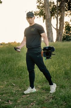 A cameraman stands in a meadow holding professional video equipment, preparing for outdoor filming.