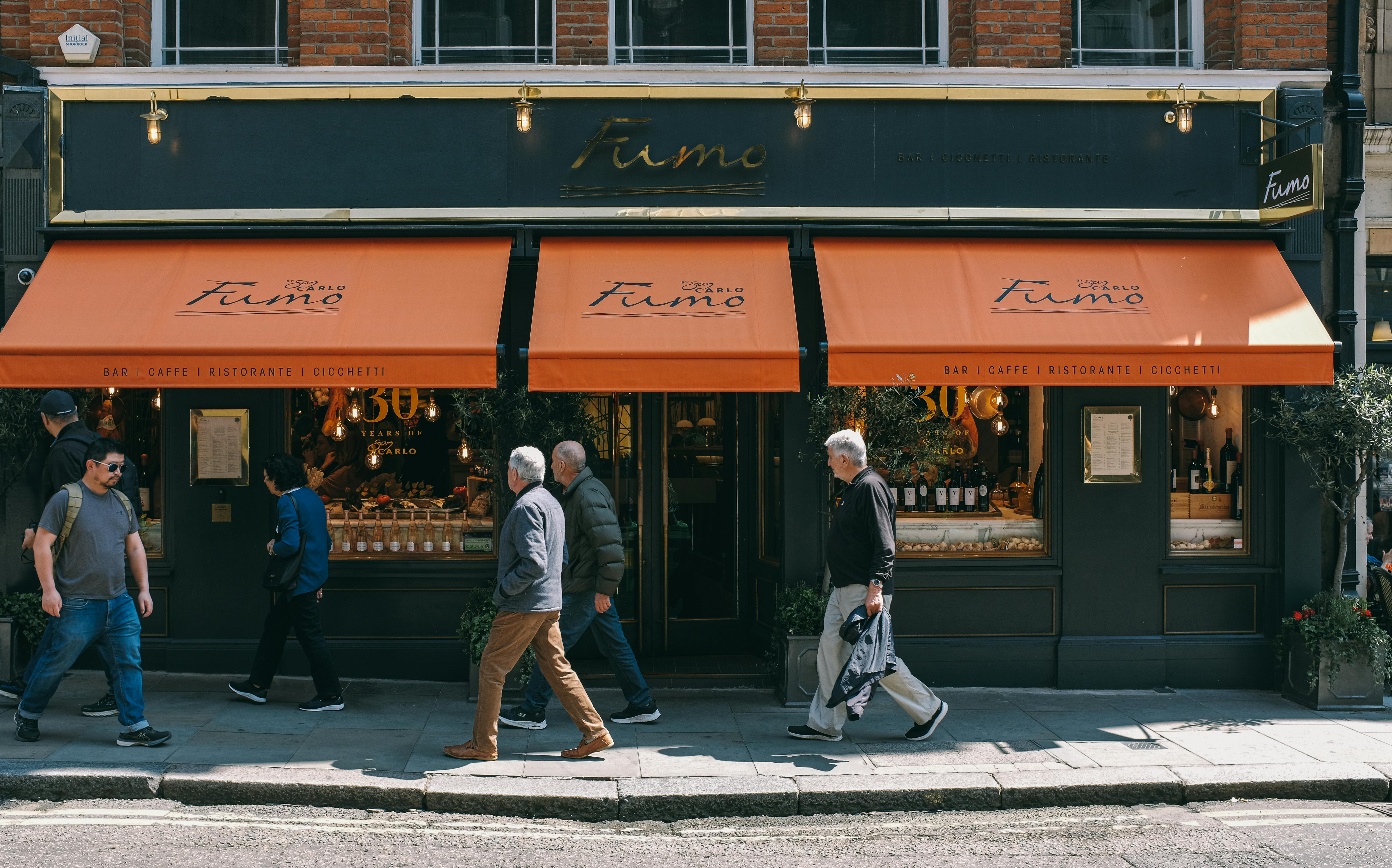 People walking past Fumo restaurant with vibrant awnings on a sunny day in London.