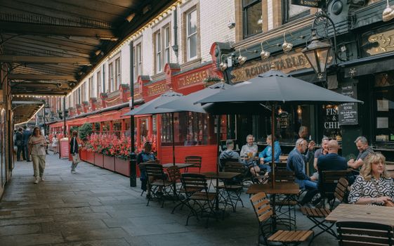 Charming London street with outdoor seating at café and pub, vibrant urban atmosphere.