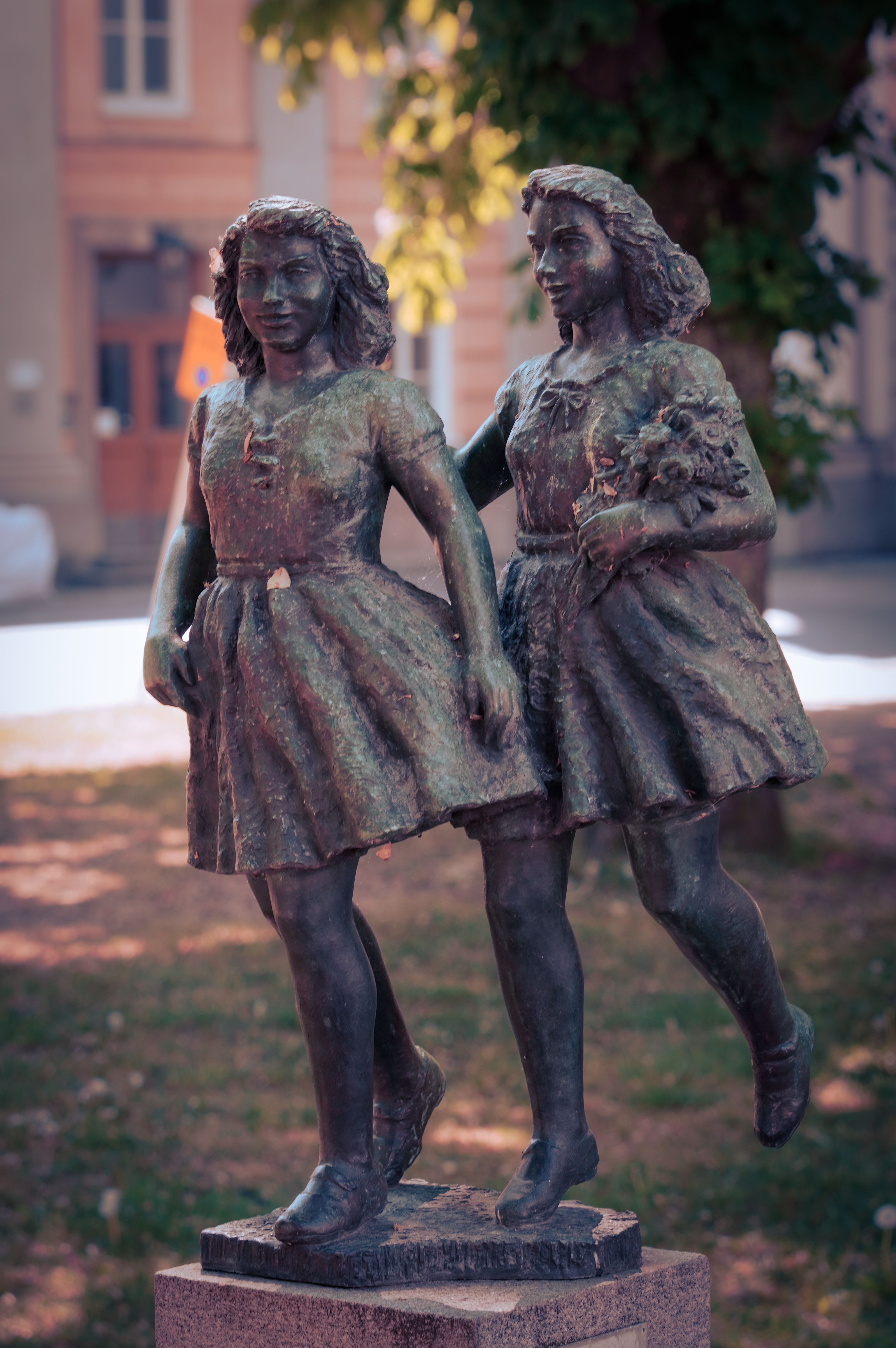 Bronze sculpture of two girls in a park setting depicting harmony and friendship.
