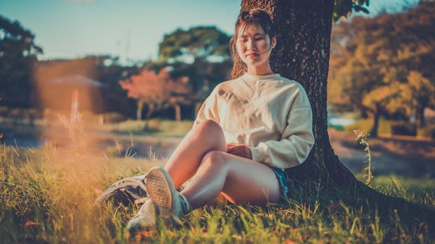 一名年轻女子静静地坐在树下，享受着户外时光，这一刻的宁静被捕捉下来