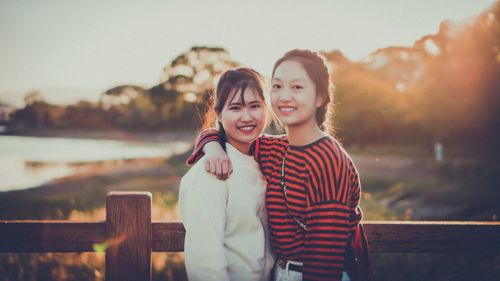 Free Two sisters embrace on a wooden bridge at sunset, capturing a warm moment of togetherness. Stock Photo