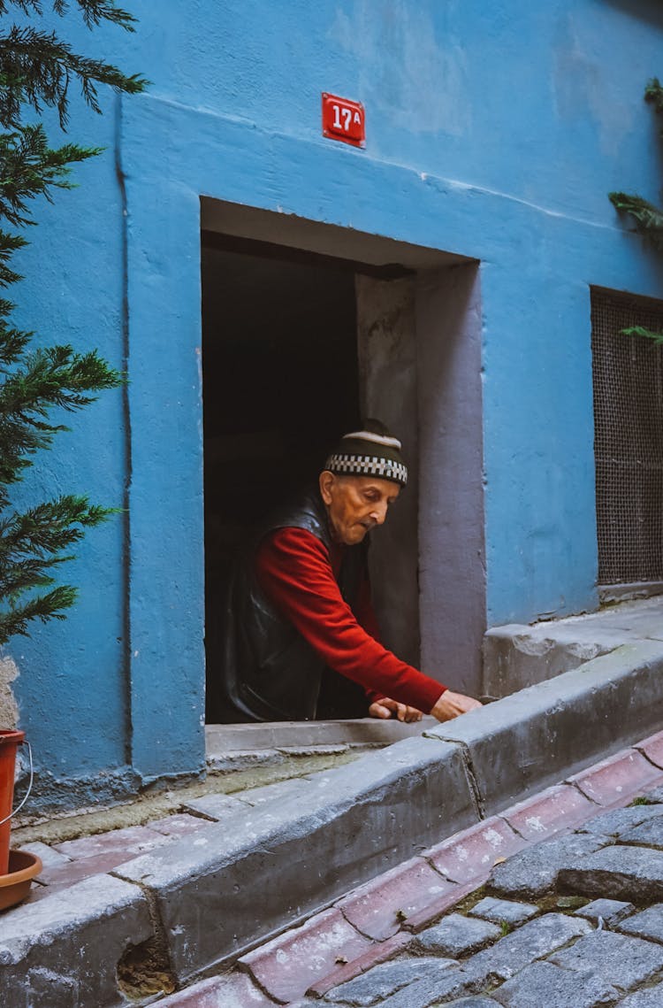 Old Man In Building Basement On Paved Street