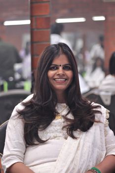 Portrait of a woman with long hair, smiling in white traditional attire, in a salon setting.