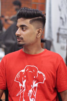 A young man in a red elephant t-shirt sits in a barbershop for a stylish haircut.