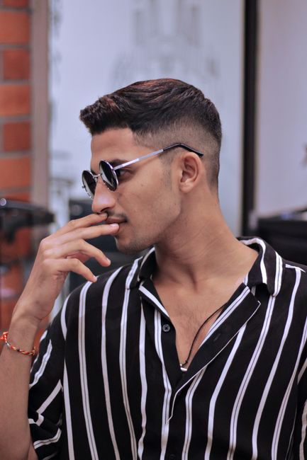 Portrait of a stylish young man wearing sunglasses and a striped shirt posing indoors.