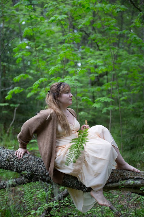 Woman Sitting on a Fallen Tree Trunk with a Fern Branch in her hand 