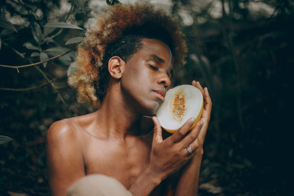 Serene portrait of a young man savoring a melon outdoors with natural surrounding.