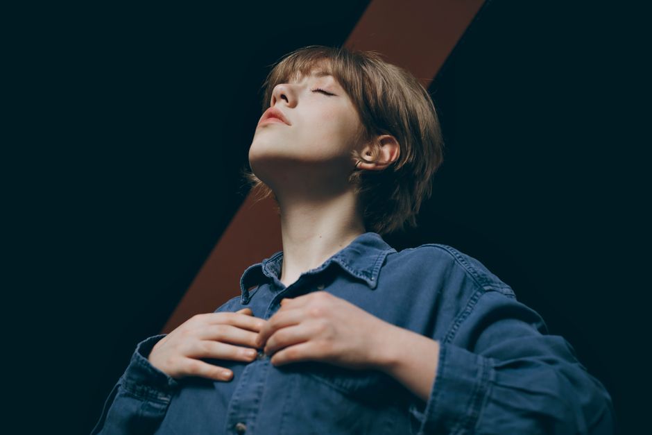 Stylish portrait of a woman wearing a denim jacket, eyes closed, in a dark setting.