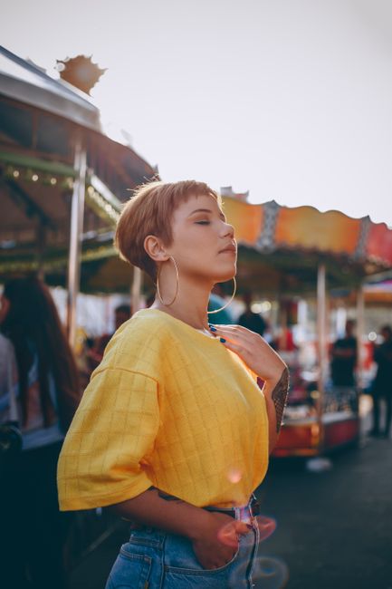 A fashionable woman basks in sunlight at an amusement park, exuding confidence and style.