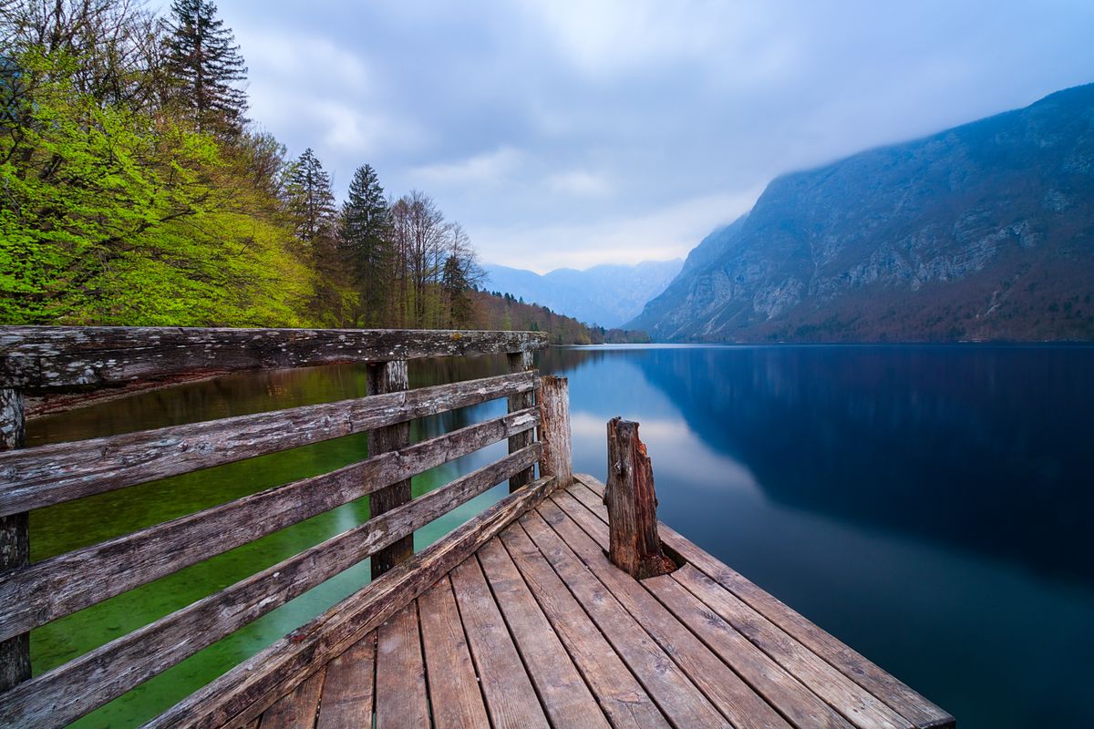 Wooden pier reaching into Lake Bohinj below forested mountains
