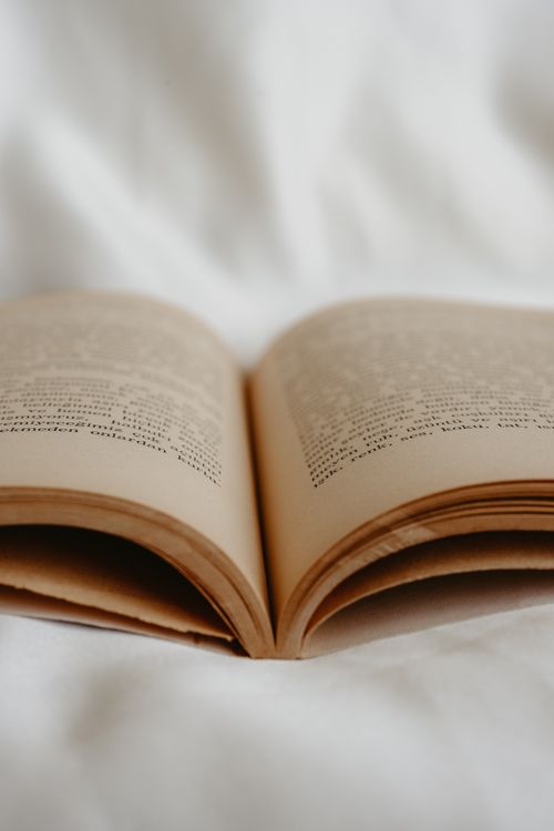 Free Detailed close-up of an open book on a white silk sheet, capturing a serene literary moment. Stock Photo