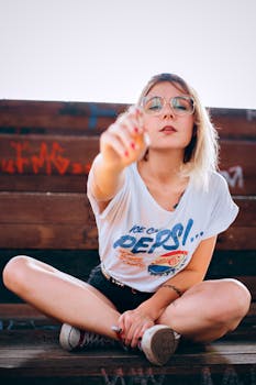 Fashionable woman with tattoos sitting on a graffiti-covered bench, showcasing casual street style in an outdoor setting.