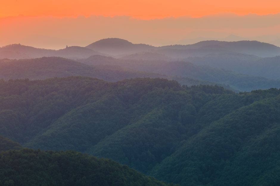 Breathtaking sunset over a forested mountain range with vibrant skies.