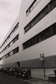 Black and white photo of a sleek modern office building facade with parked scooters.
