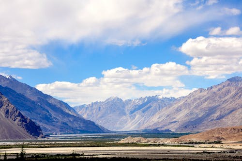View of a Valley and Rocky Mountain Range under Blue Sky with White Clouds 