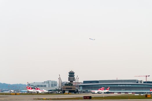 Swiss airplanes at Zurich Airport with control tower and terminal in background.