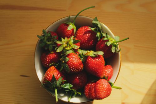 Free A vibrant top view of fresh strawberries in a bowl on a wooden table, sunlight casting shadows. Stock Photo