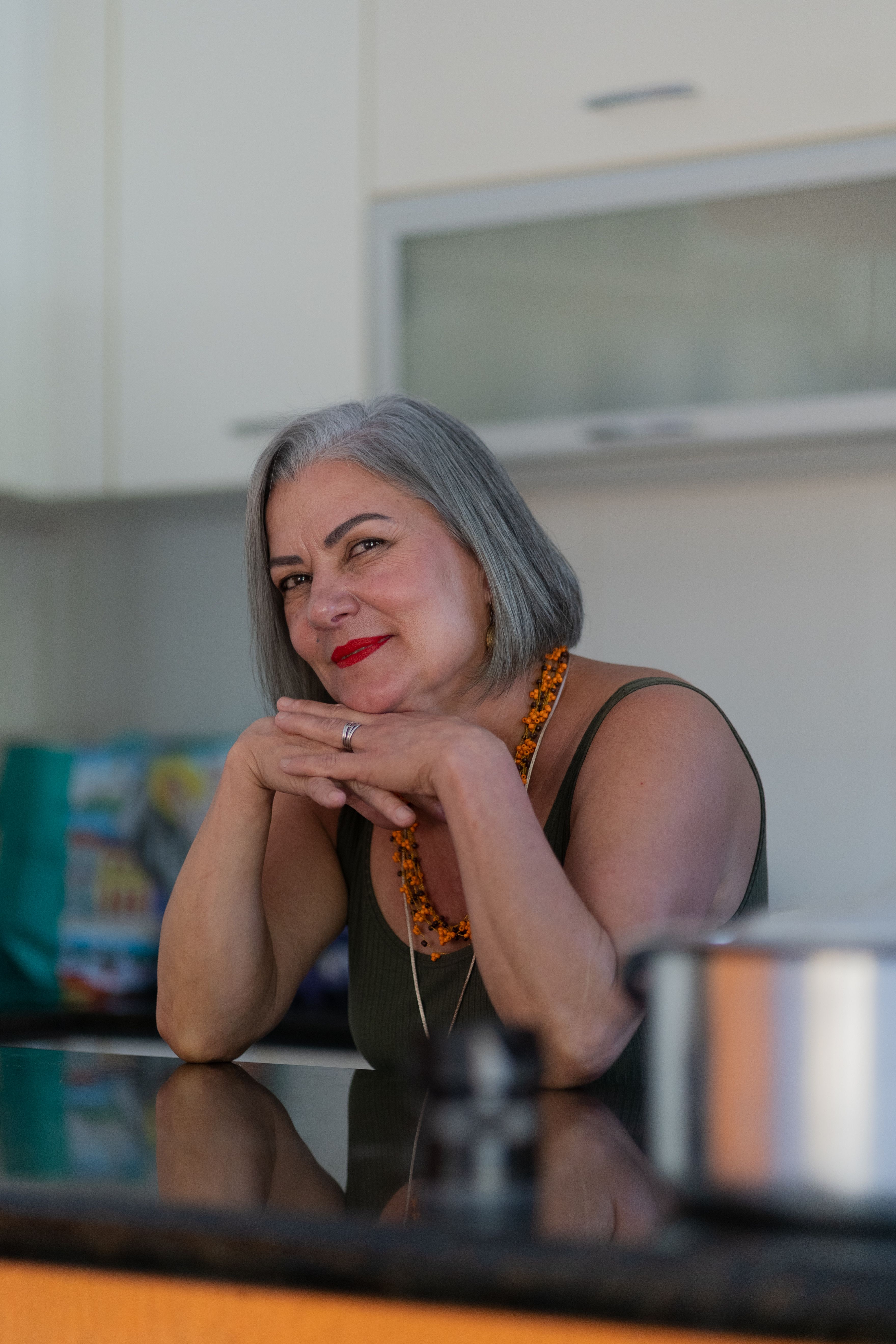 Portrait of a confident senior woman with red lipstick posing in a modern kitchen setting.