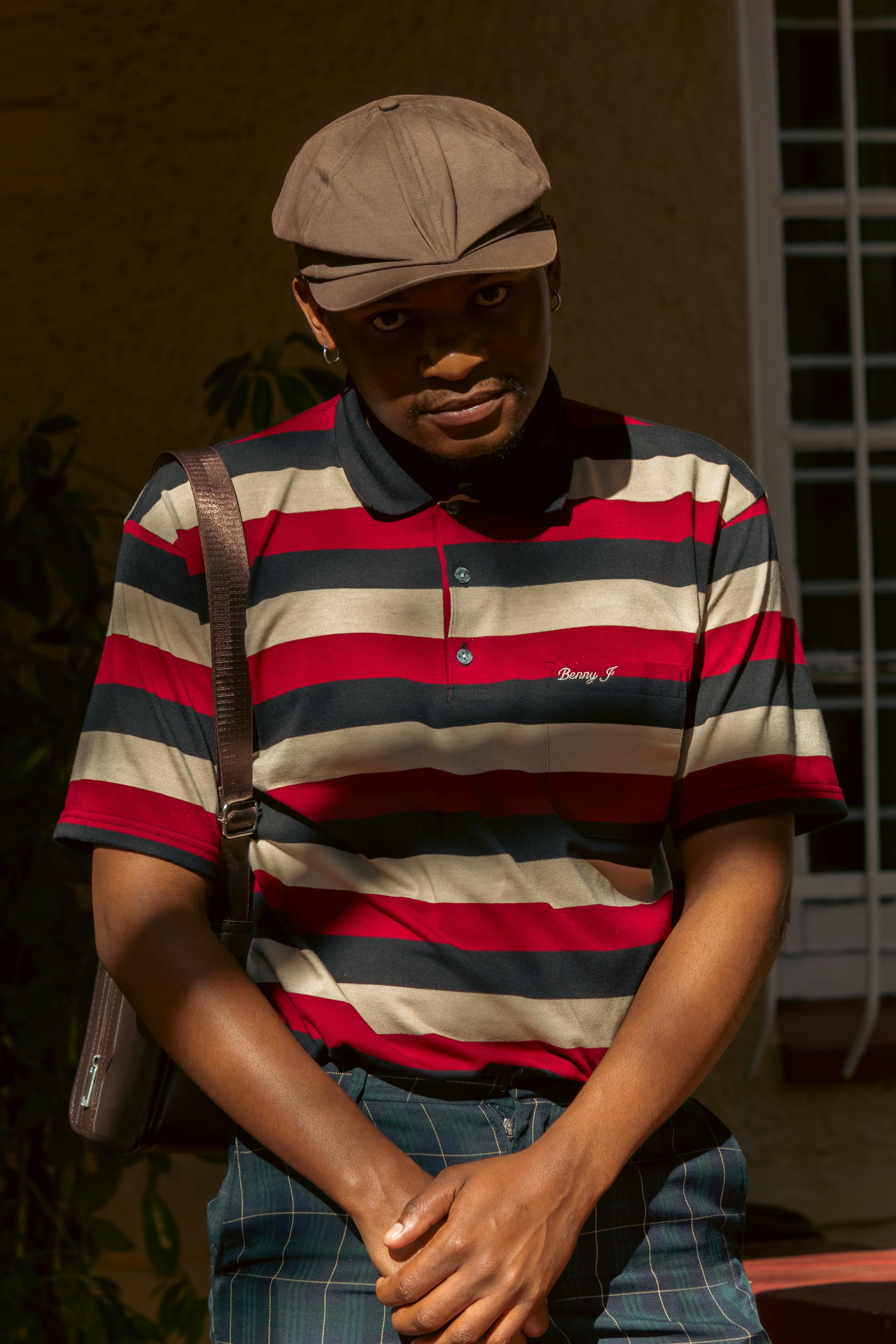 Portrait of a man in striped polo shirt and ivy cap outdoors.