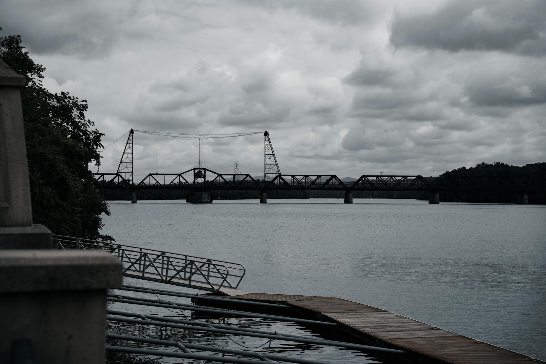 Moody riverscape featuring a suspension bridge under a clouded sky.