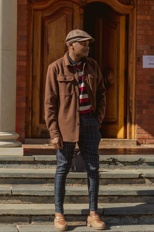 Free Elegant man with fedora and plaid pants against wooden doors. Stylish fall outfit. Stock Photo