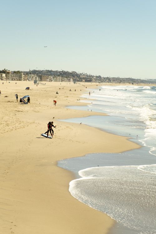 Free A serene beach scene featuring surfers and gentle waves under a clear sky. Stock Photo