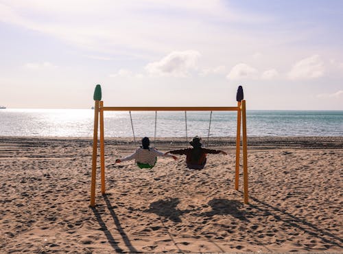 Two Girls Rocking on Swings at a Sunny Beach