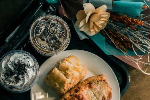Top view of iced coffee with pastries on a plate, accompanied by flowers, on a tray.