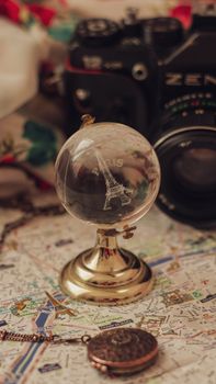 A vintage glass globe featuring the Eiffel Tower and Paris on an antique map with a classic camera.