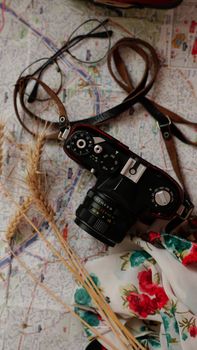 A vintage camera with straps on a map, surrounded by dried wheat and floral fabric.