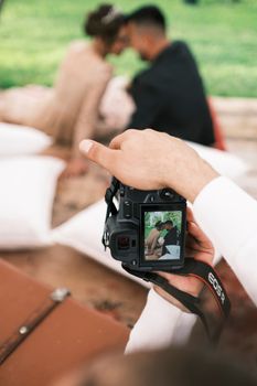 A photographer capturing a couple's intimate moment through a camera outdoors.