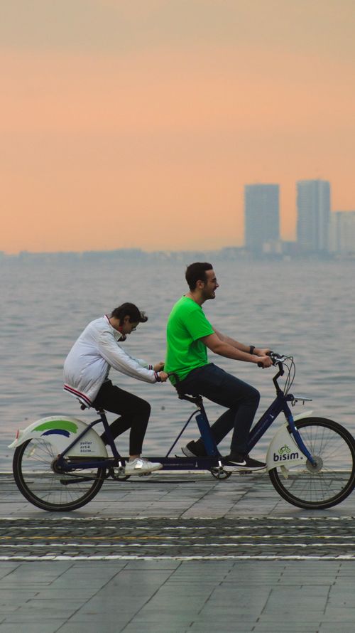 Free Couple riding tandem bike at sunset along İzmir's waterfront promenade. Stock Photo