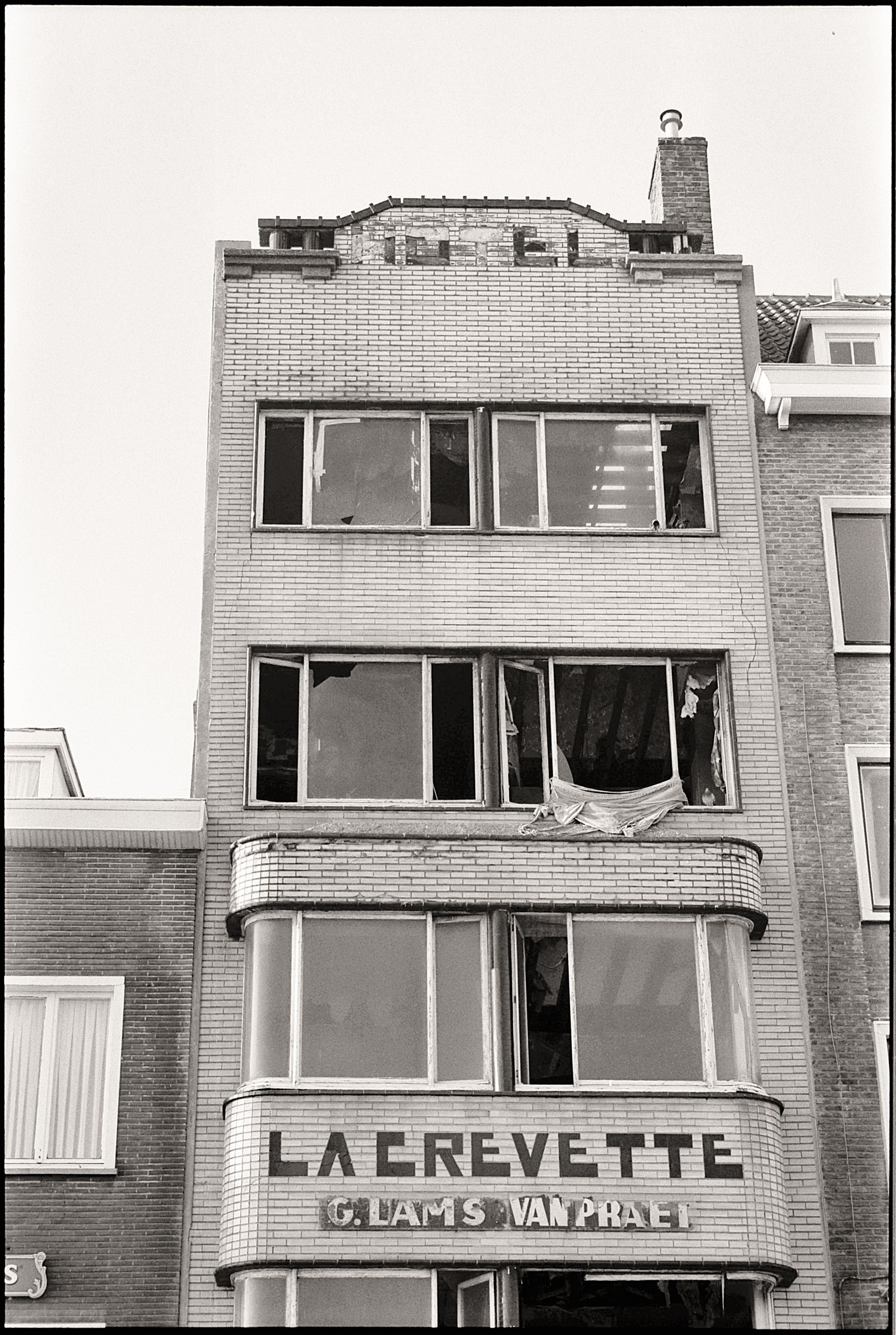 Black and white photo of an urban townhouse facade with broken windows, creating an eerie mood.