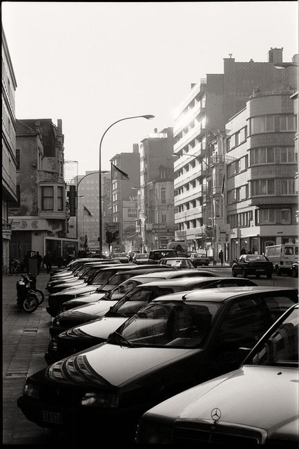 Black and white street photo of a cityscape with parked cars and urban architecture.