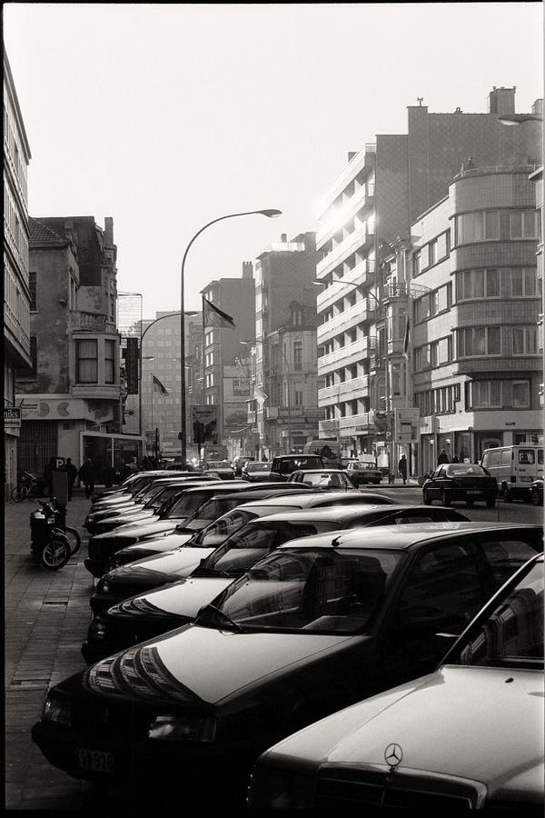 Foto de rua em preto e branco de uma paisagem urbana com carros estacionados e arquitetura urbana.