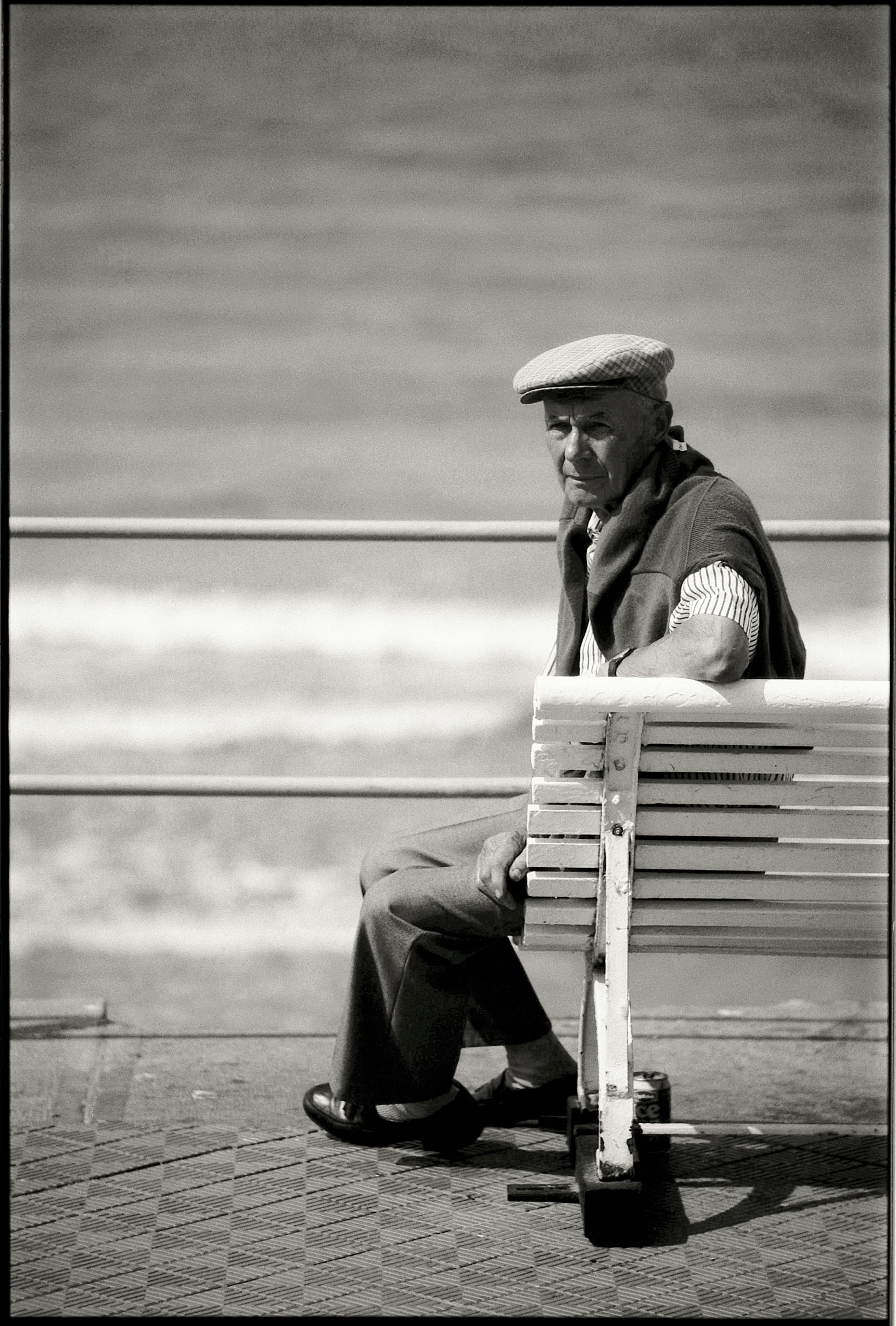 Elderly man sitting on a bench by the sea, captured in a monochrome palette.