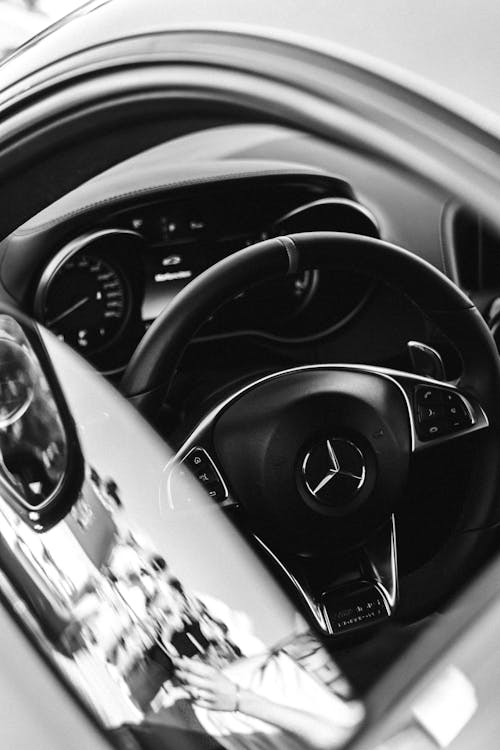 Black and White Photo of Cars Dashboard and Steering Wheel seen through Open Window
